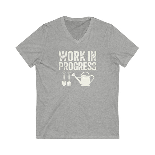 Athletic Light Heather Gray vneck t-shirt with white words that say 'Work in Progress' in distressed style text. Below the words are graphic images of gardening tools including a shovel, pitchfork and watering can.