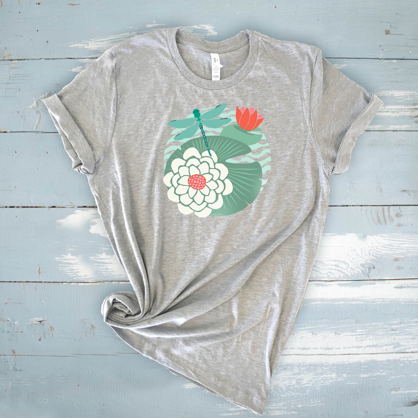 Illustrated dragonfly hovering over a green lily pad with pink and white water lily flowers on a calm pond, printed on a soft athletic gray colored crewneck t-shirt.