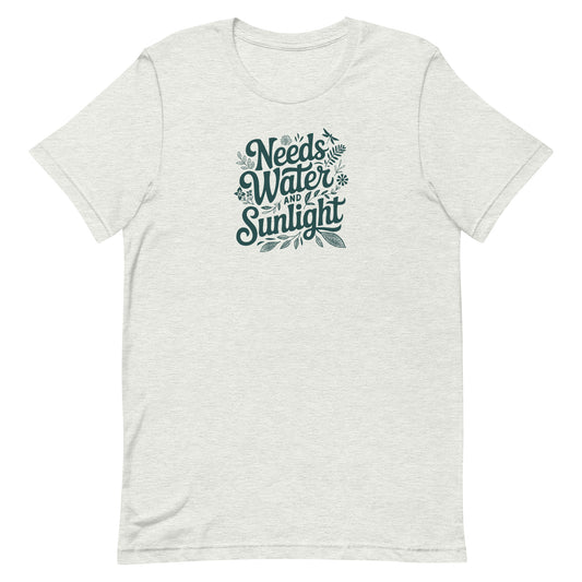 Pale Athletic gray colored crewneck t-shirt with dark green words that say 'Needs Water and Sunlight' in script style text with dragonfly, flower and leaf illustrations around the words.
