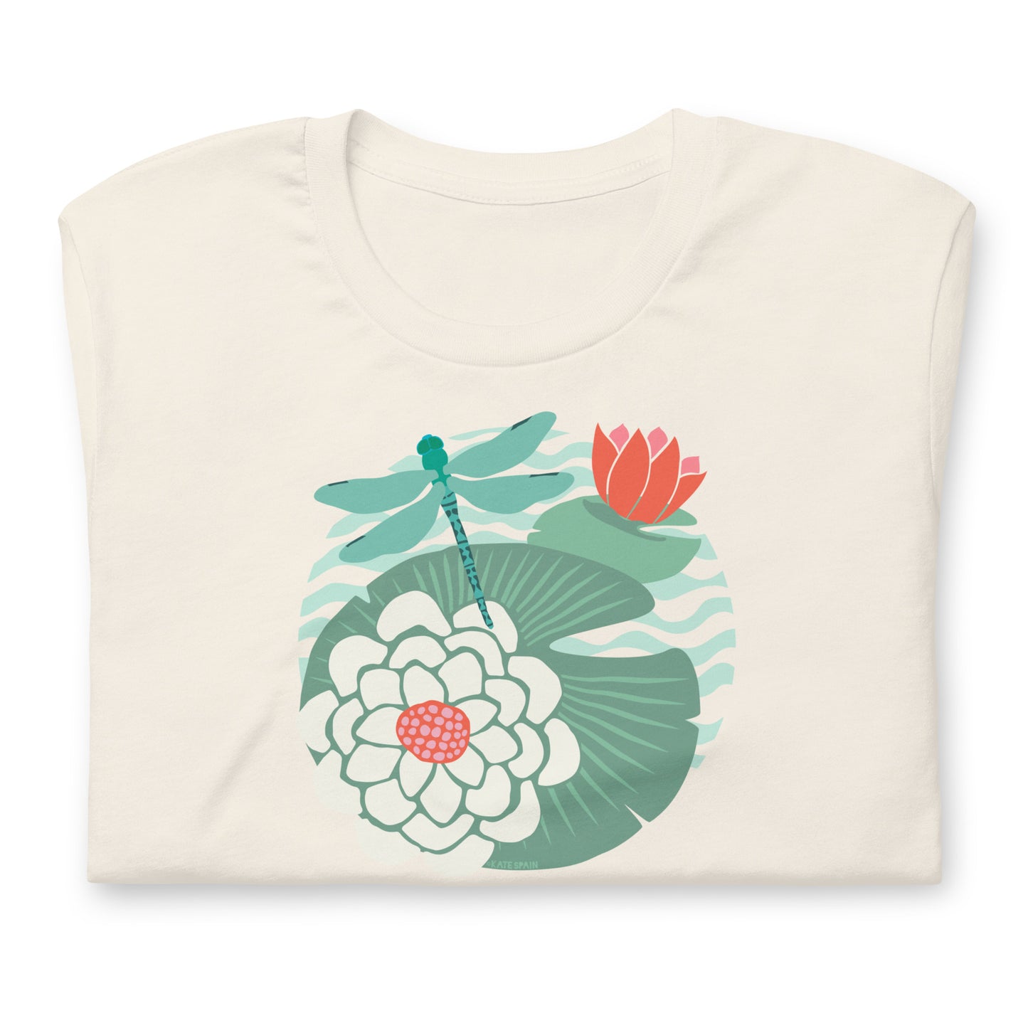 Illustrated dragonfly hovering over a green lily pad with pink and white water lily flowers on a calm pond, printed on a soft off-white cream colored premium quality crewneck t-shirt. Shown folded for scale.