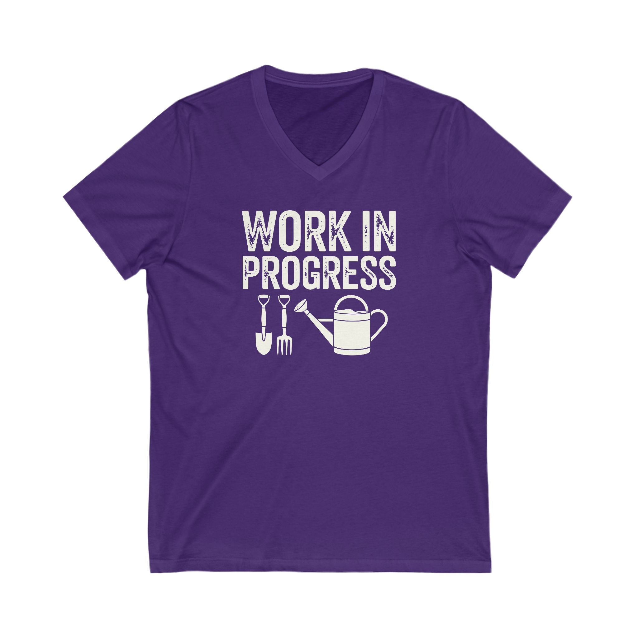 Rich purple colored vneck t-shirt with white words that say 'Work in Progress' in distressed style text. Below the words are graphic images of gardening tools including a shovel, pitchfork and watering can.