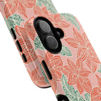 Hibiscus Coral MagSafe iPhone 17 Glossy Case — angled view showing slim profile; blush pink case with coral red hibiscus flowers and teal-green leaves in bold botanical linework
