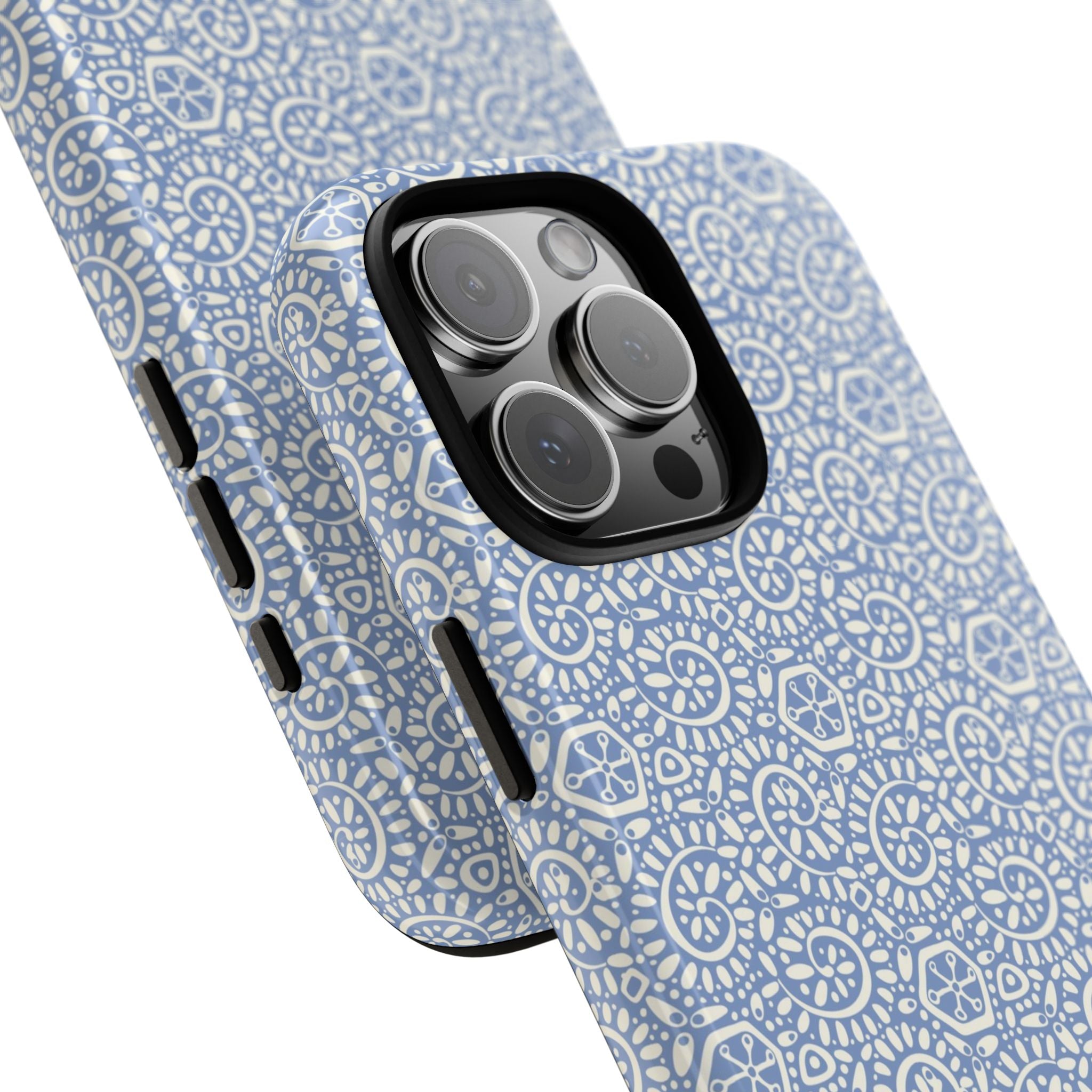 Canto Swirls Mist iPhone 16 Pro Max Glossy Case — angled view showing slim profile; periwinkle blue folk-art medallion pattern of radiating white circular motifs, dot clusters, and geometric centers