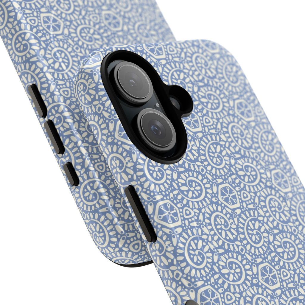 Canto Swirls Mist MagSafe iPhone 17 Glossy Case — angled view showing slim profile; periwinkle blue folk-art medallion pattern of radiating white circular motifs, dot clusters, and geometric centers