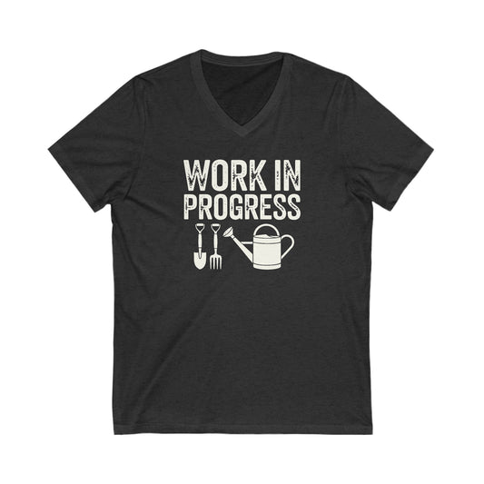 Charcoal Gray vneck t-shirt with white words that say 'Work in Progress' in distressed style text. Below the words are graphic images of gardening tools including a shovel, pitchfork and watering can.