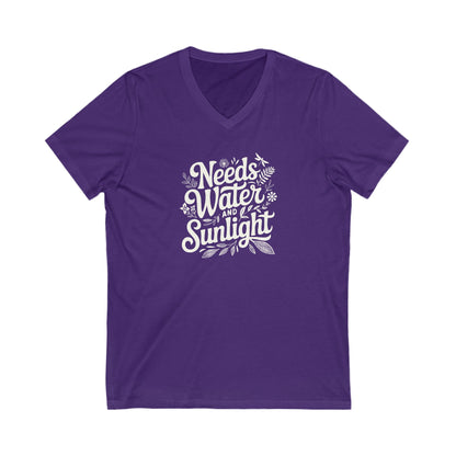 Saturated purple colored vneck t-shirt with white words that say 'Needs Water and Sunlight' in script style text with dragonfly, flower and leaf illustrations around the words.