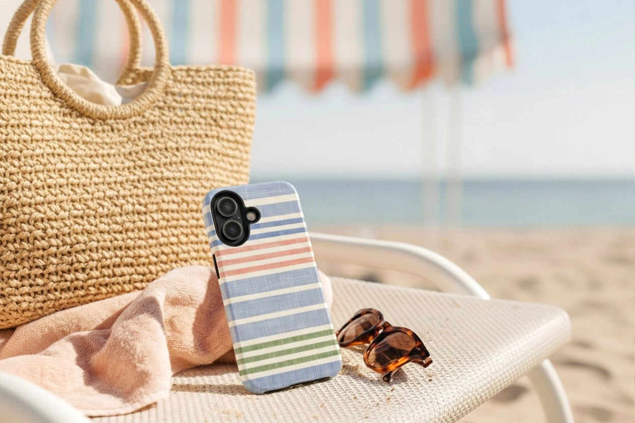 Phone case with striped design on a beach chair with a straw bag and sunglasses.