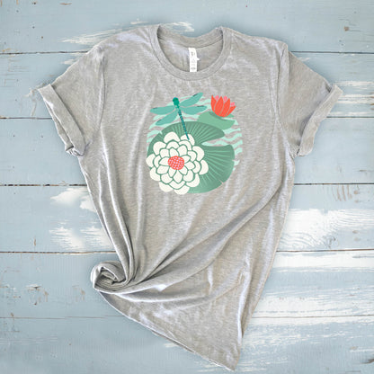 Illustrated dragonfly hovering over a green lily pad with pink and white water lily flowers on a calm pond, printed on a soft athletic gray colored crewneck t-shirt.