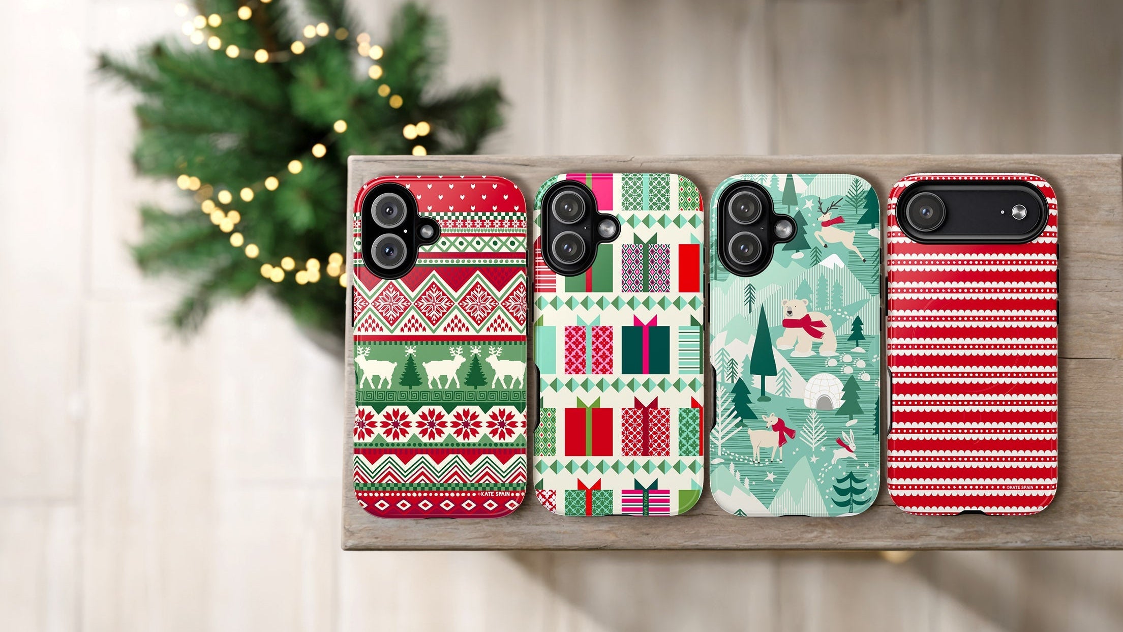 Four Christmas-themed phone cases on a wooden surface with a blurred decorative background.