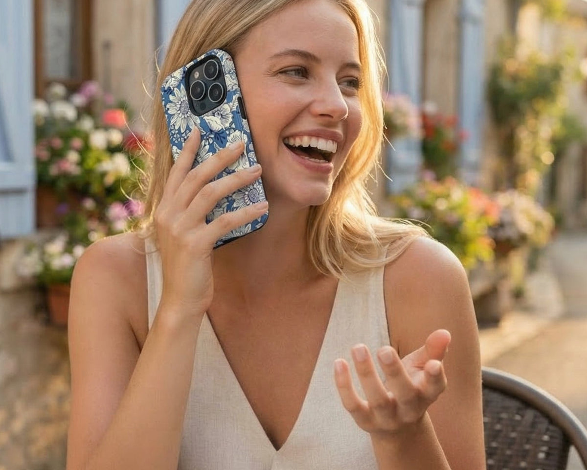 Woman sitting at an outdoor cafe laughing and talking happily on a floral iphone 17 case