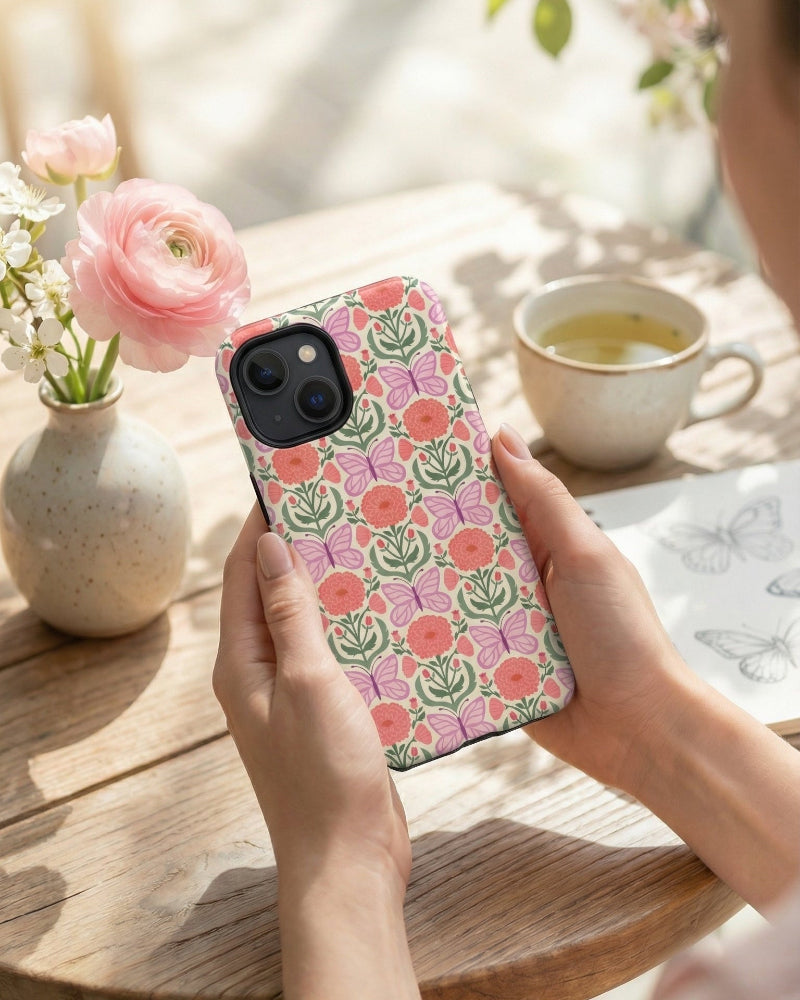Person holding a phone with a floral case in a cozy setting with flowers and tea.