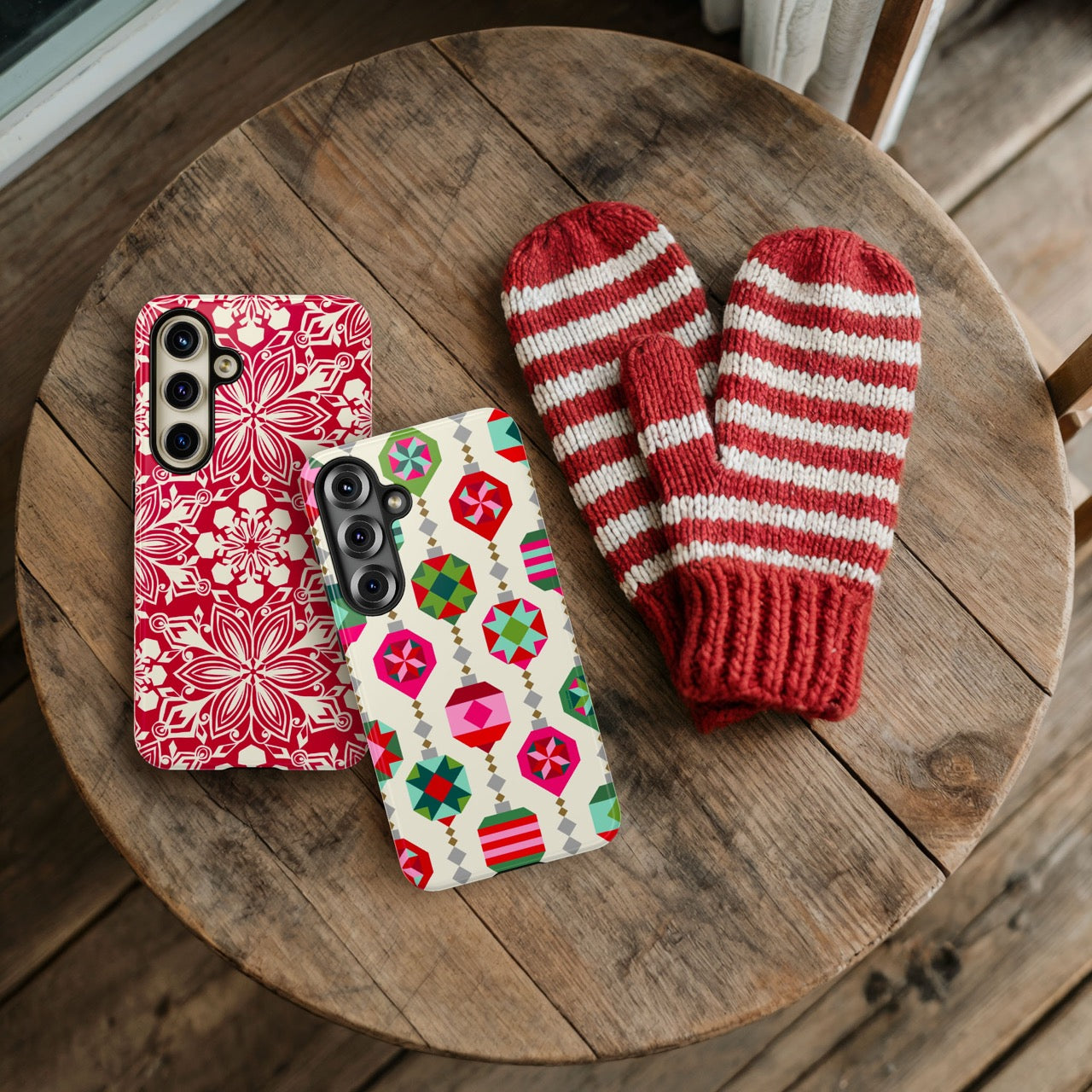 Two patterned phone cases and a pair of red and white striped mittens on a wooden surface.