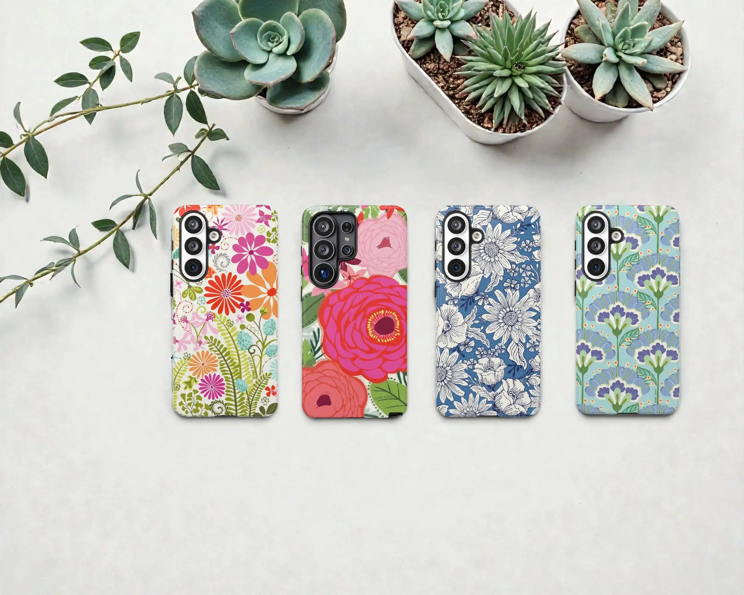 Four floral-patterned phone cases on a white surface with plants in the background.