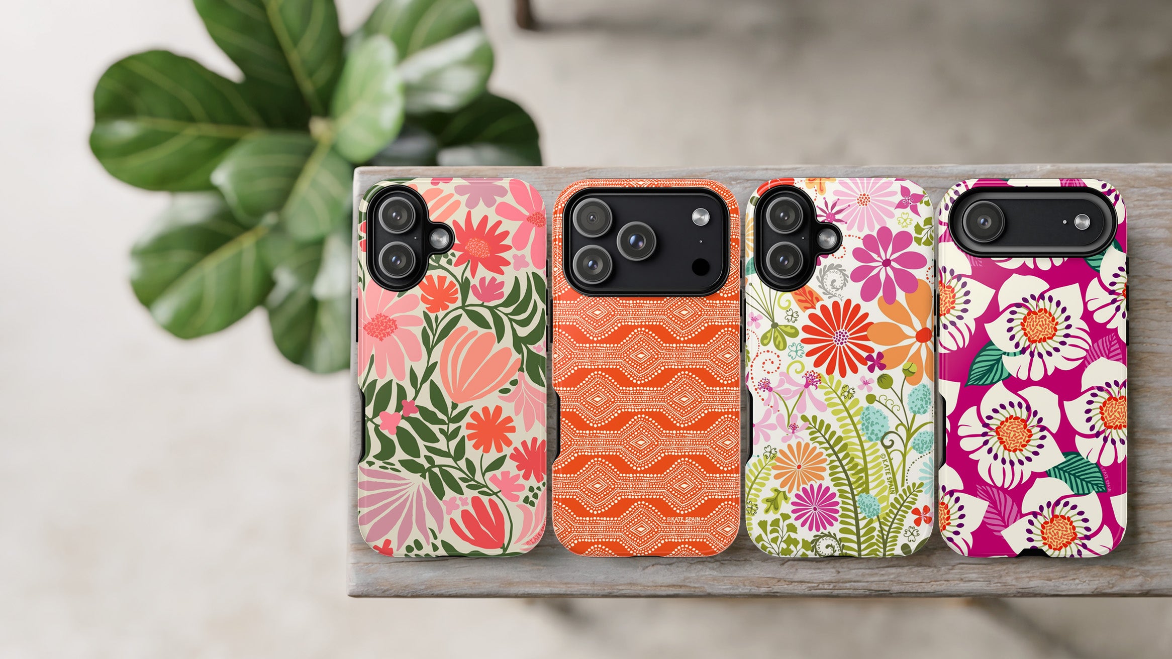 Four floral phone cases on a wooden surface with a plant in the background