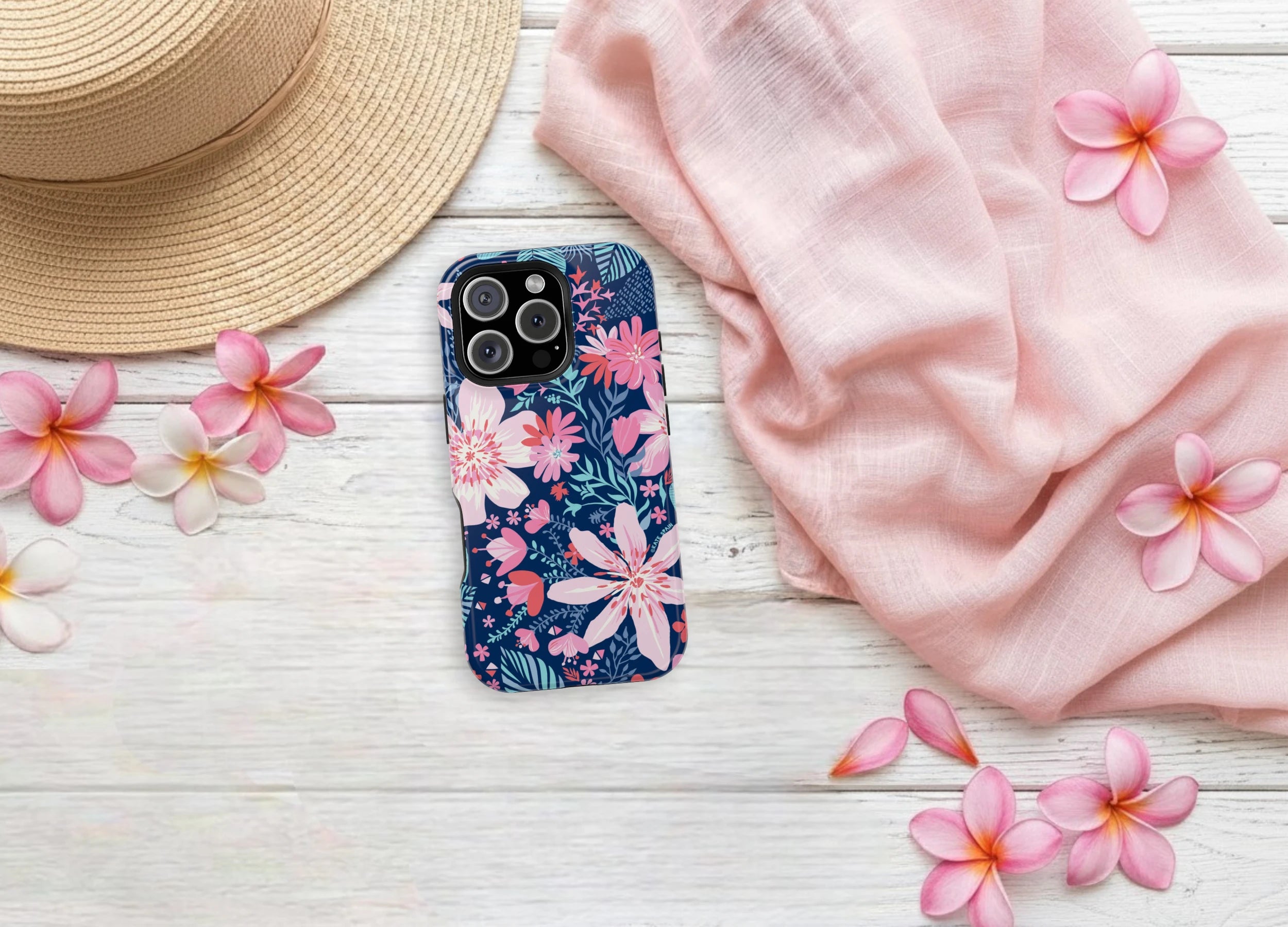 Phone case with pink tropical floral design on a wooden surface with flowers and a hat.