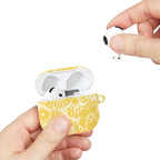 floriori AirPods case with sophisticated and energetic hand painted flower silhouettes. yellow floral on a cream glossy background. showing scale with earbuds.