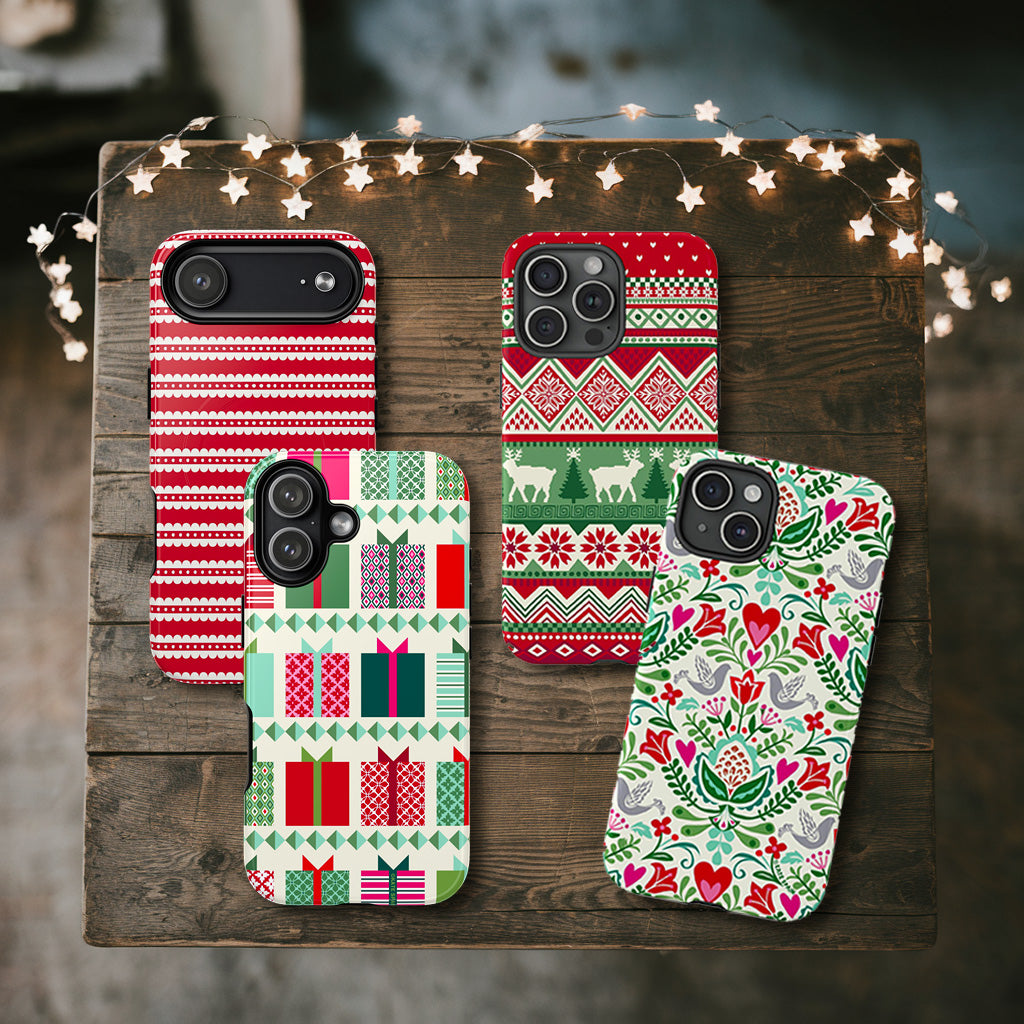 Four festive phone cases on a wooden surface with string lights.