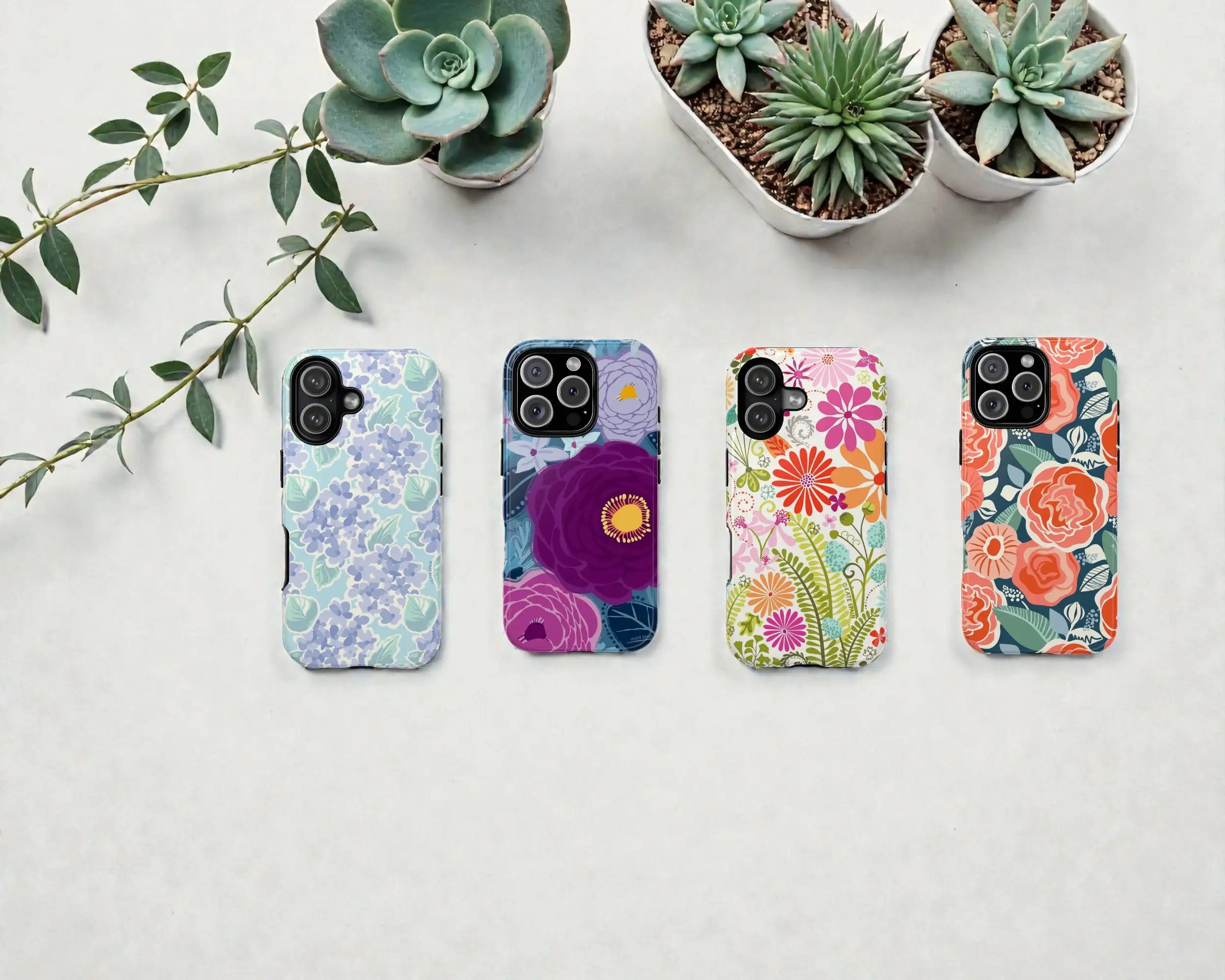 Four floral-patterned phone cases on a light surface with plants in the background