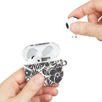 floriori AirPods case with sophisticated and energetic hand painted flower silhouettes. black floral on a cream glossy background. shows scale