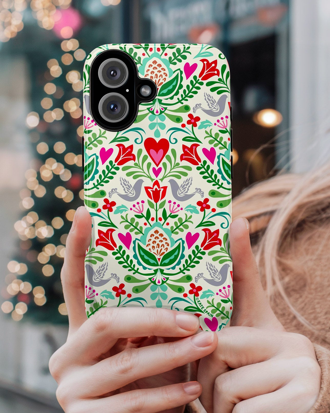 Christmas phone case with colorful floral and heart pattern held by a person against a blurred festive background