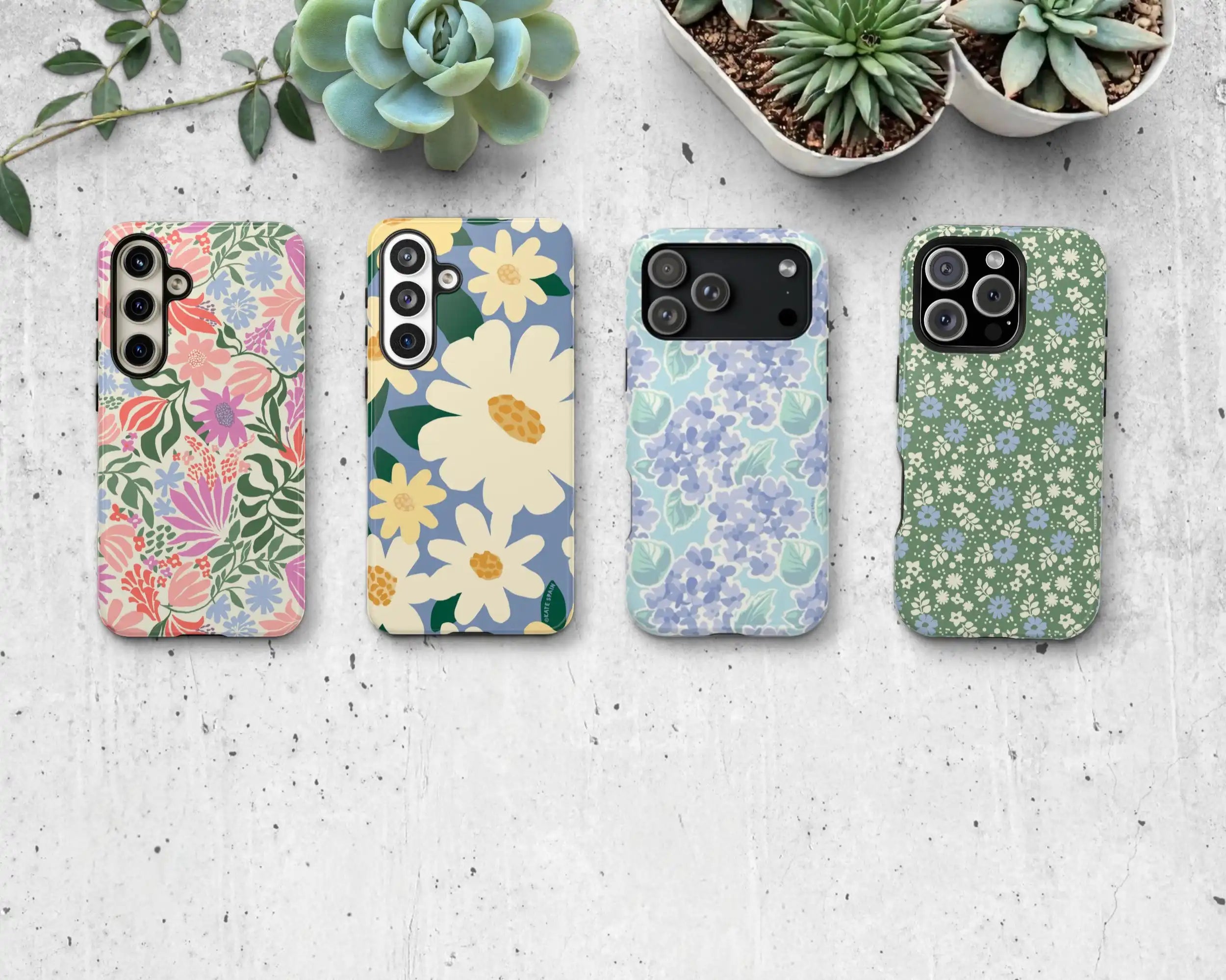 Four floral-patterned phone cases on a textured surface with plants in the background.