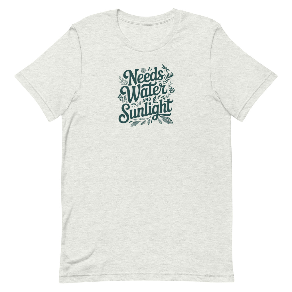 Pale Athletic gray colored crewneck t-shirt with dark green words that say 'Needs Water and Sunlight' in script style text with dragonfly, flower and leaf illustrations around the words.
