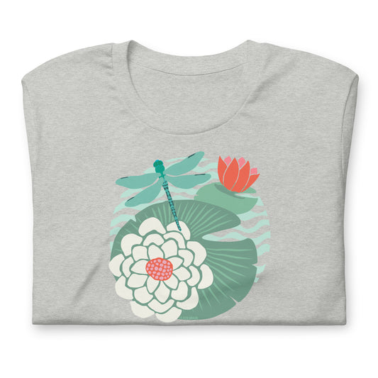 Illustrated dragonfly hovering over a green lily pad with pink and white water lily flowers on a calm pond, printed on a soft unisex t-shirt.