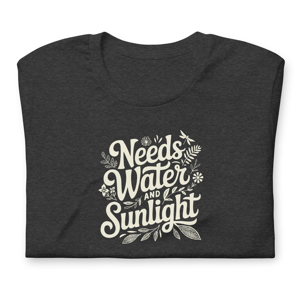 Dark charcoal gray heather colored crewneck t-shirt with white words that say 'Needs Water and Sunlight' in script style text with dragonfly, flower and leaf illustrations around the words.
