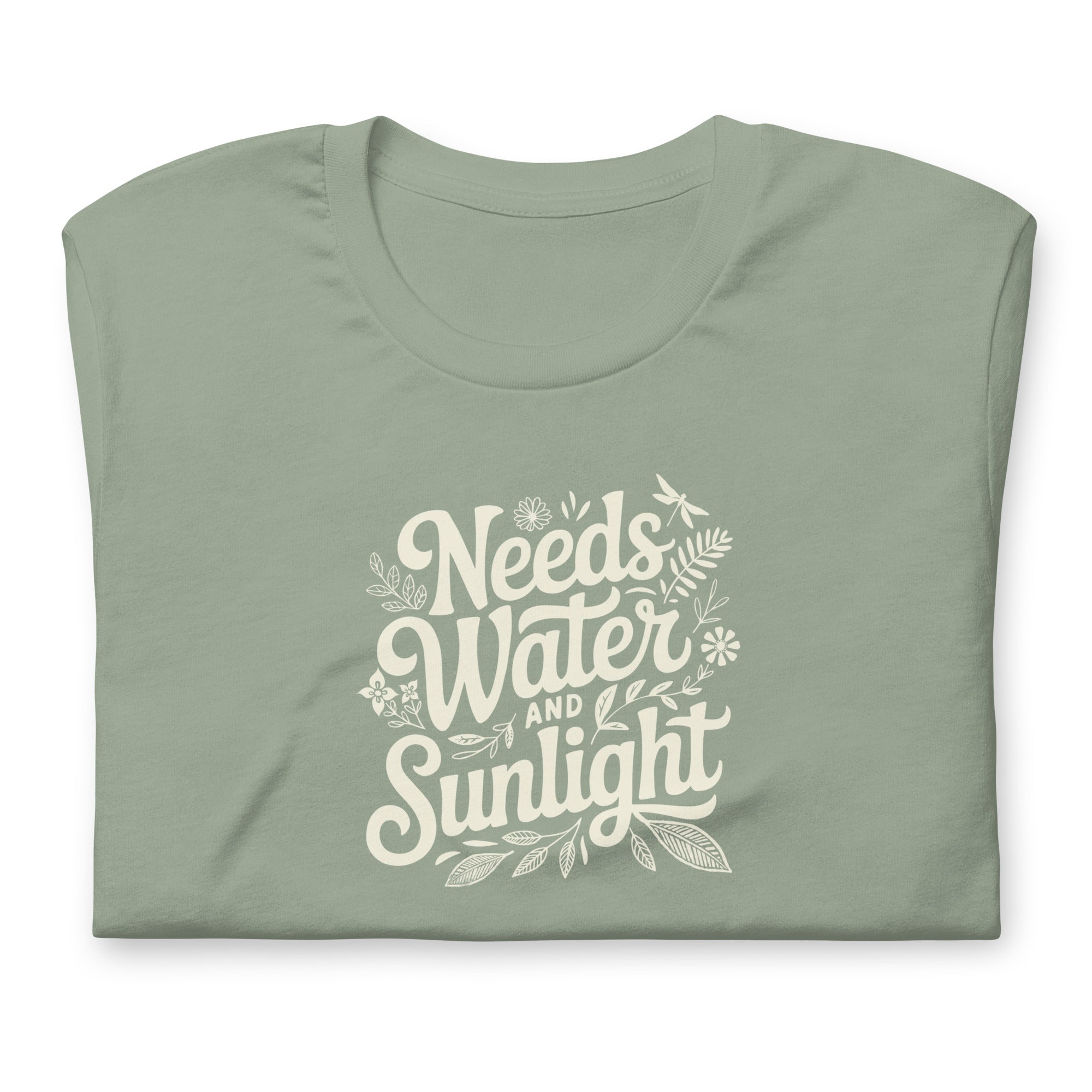 Pale sage green colored crewneck t-shirt with white words that say 'Needs Water and Sunlight' in script style text with dragonfly, flower and leaf illustrations around the words.