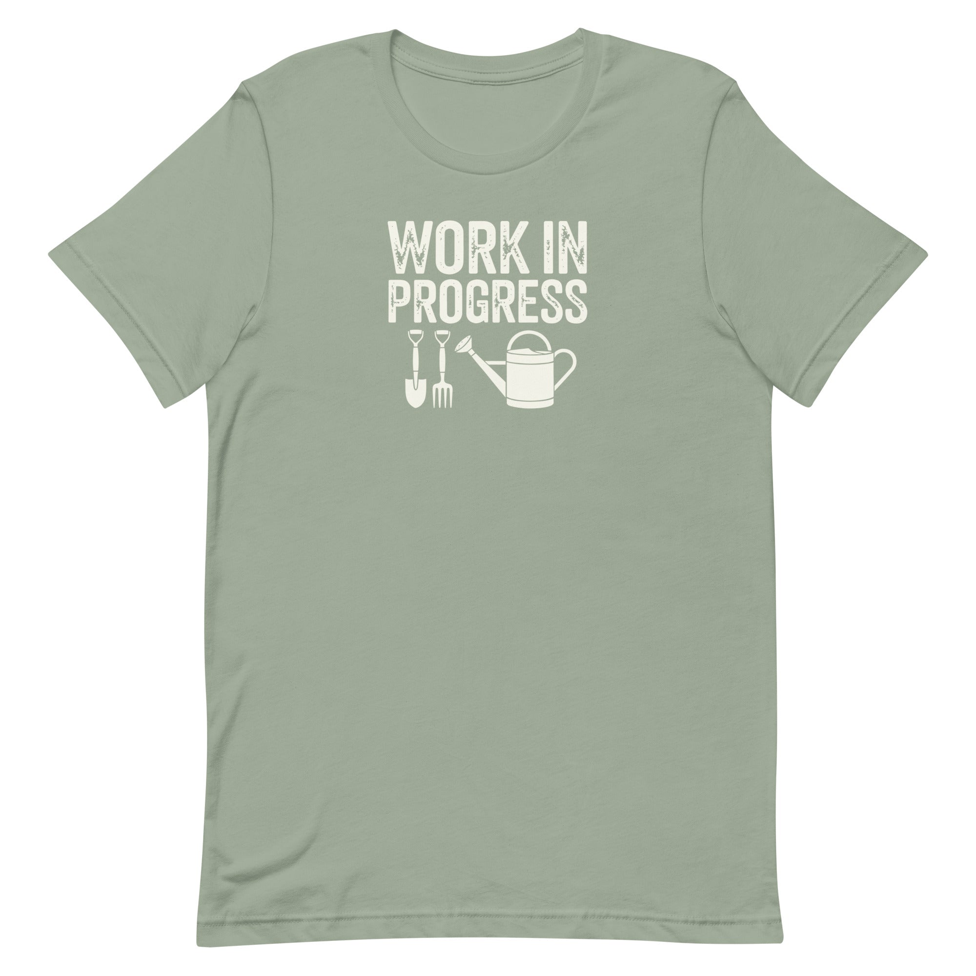 “Work in Progress” gardening graphic with shovel, pitchfork, and watering can printed in white on a soft sage green colored crewneck t-shirt.