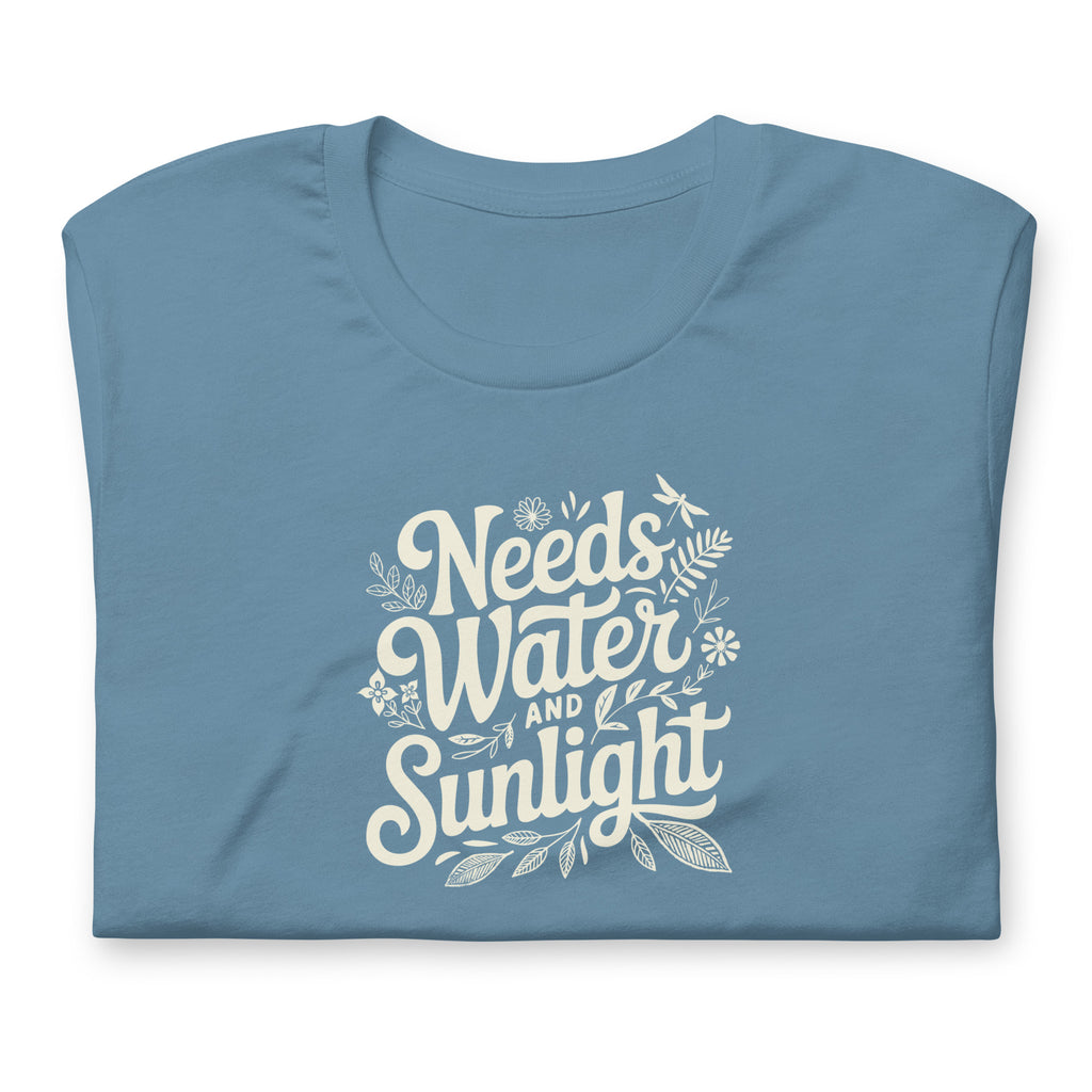 Steel blue colored crewneck t-shirt with white words that say 'Needs Water and Sunlight' in script style text with dragonfly, flower and leaf illustrations around the words.