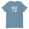 “Work in Progress” gardening graphic with shovel, pitchfork, and watering can printed in white on a soft steel blue colored crewneck t-shirt.