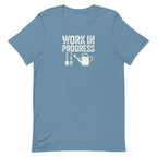 “Work in Progress” gardening graphic with shovel, pitchfork, and watering can printed in white on a soft steel blue colored crewneck t-shirt.